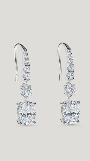Staple pair of drop earrings for women featuring stunning oval cut stones accented with tapered round brilliant stones.